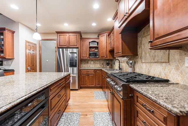 kitchen with light stone counters, stainless steel appliances, sink, light hardwood / wood-style flooring, and hanging light fixtures