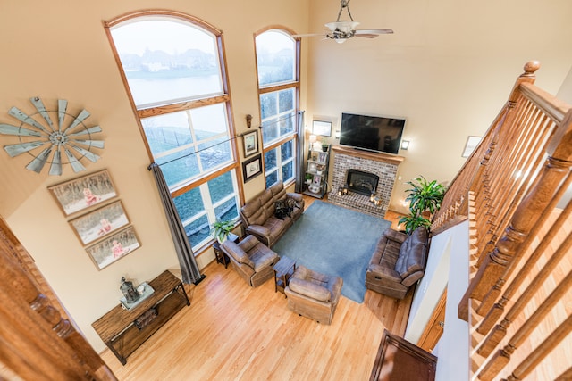 living room featuring a fireplace, hardwood / wood-style floors, ceiling fan, and a high ceiling