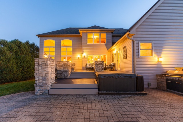 back house at dusk featuring a patio, an outdoor kitchen, a hot tub, and a deck