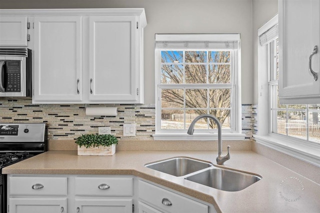 kitchen with tasteful backsplash, sink, white cabinets, and appliances with stainless steel finishes