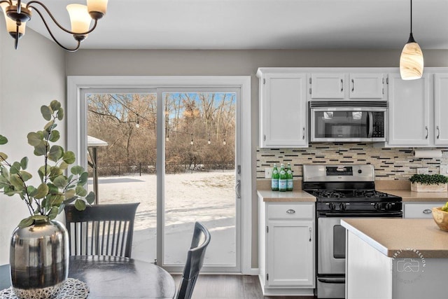 kitchen featuring decorative light fixtures, tasteful backsplash, white cabinetry, stainless steel appliances, and light wood-type flooring