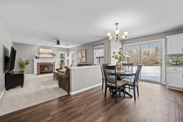 dining space featuring a brick fireplace, ceiling fan with notable chandelier, and dark hardwood / wood-style flooring