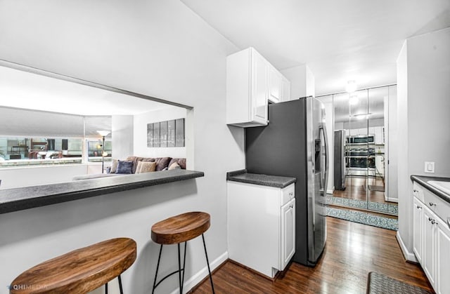 kitchen with a breakfast bar, stainless steel appliances, white cabinetry, and dark wood-type flooring