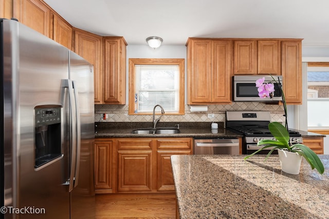 kitchen featuring backsplash, sink, dark stone countertops, light wood-type flooring, and appliances with stainless steel finishes