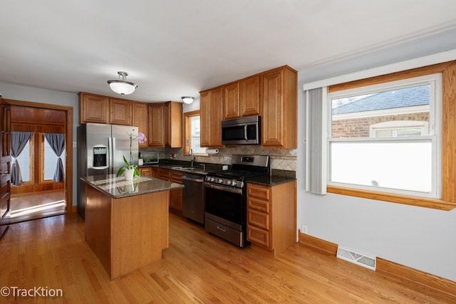 kitchen featuring a center island, stainless steel appliances, tasteful backsplash, dark stone countertops, and light wood-type flooring