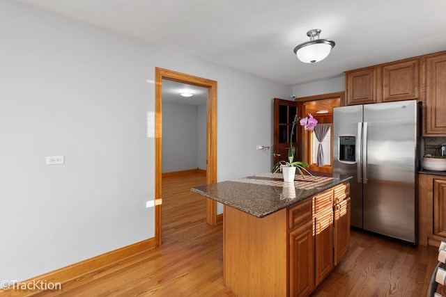 kitchen with a center island, a kitchen breakfast bar, stainless steel refrigerator with ice dispenser, dark stone countertops, and wood-type flooring