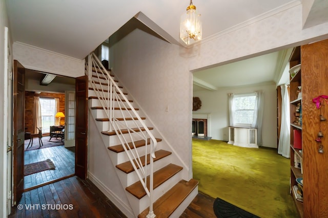 staircase featuring a notable chandelier, a fireplace, wood-type flooring, and ornamental molding