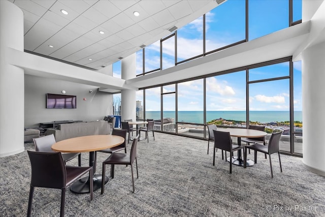 carpeted dining area with a high ceiling and a water view