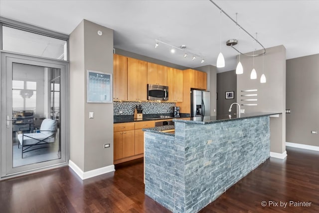 kitchen with decorative backsplash, appliances with stainless steel finishes, pendant lighting, dark hardwood / wood-style floors, and an island with sink