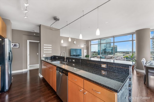 kitchen featuring dark hardwood / wood-style flooring, dark stone counters, stainless steel appliances, a kitchen island with sink, and sink