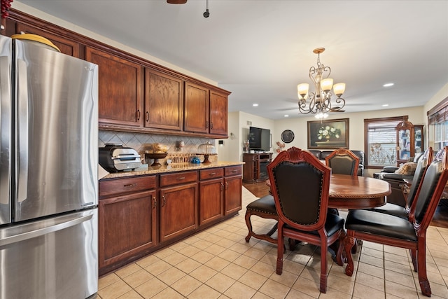 kitchen with decorative backsplash, stainless steel fridge, light tile patterned floors, a notable chandelier, and light stone counters