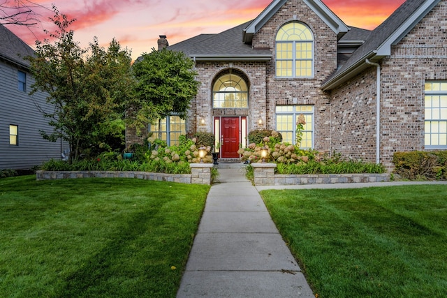 exterior entry at dusk with a yard, brick siding, and a chimney