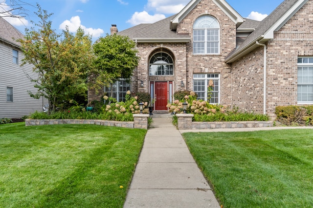 doorway to property featuring a shingled roof, brick siding, a yard, and a chimney