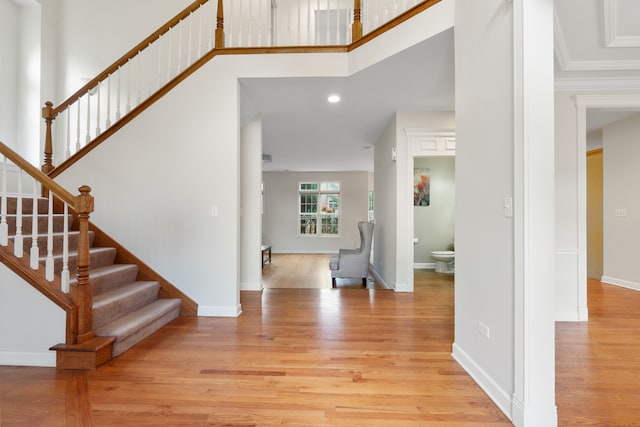 foyer entrance featuring stairway, baseboards, a towering ceiling, and light wood finished floors