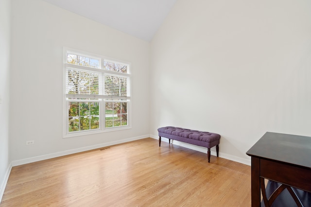 living area featuring light wood-type flooring, visible vents, lofted ceiling, and baseboards