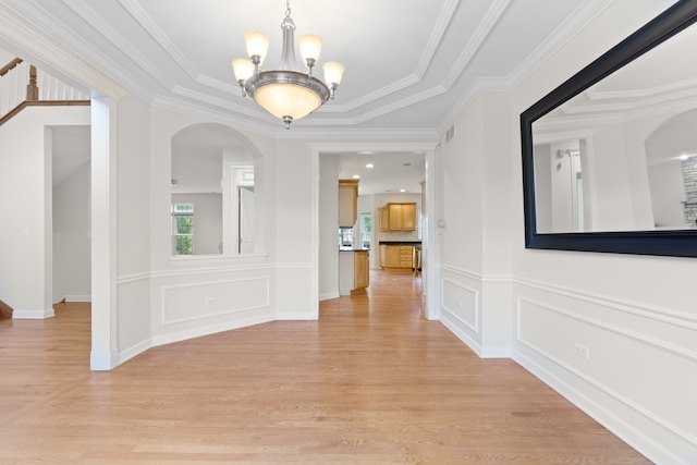 hallway featuring a chandelier, crown molding, light wood-type flooring, and a decorative wall