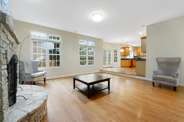 living area with a stone fireplace, light wood-type flooring, recessed lighting, and baseboards