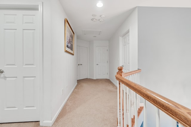 corridor featuring attic access, baseboards, light colored carpet, and an upstairs landing