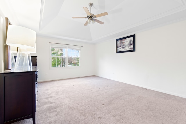 unfurnished bedroom with lofted ceiling, light carpet, a raised ceiling, ceiling fan, and ornamental molding