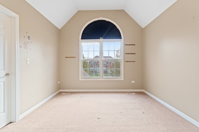 spare room with light carpet, vaulted ceiling, and baseboards