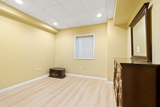 empty room with baseboards, a paneled ceiling, and light wood-style floors