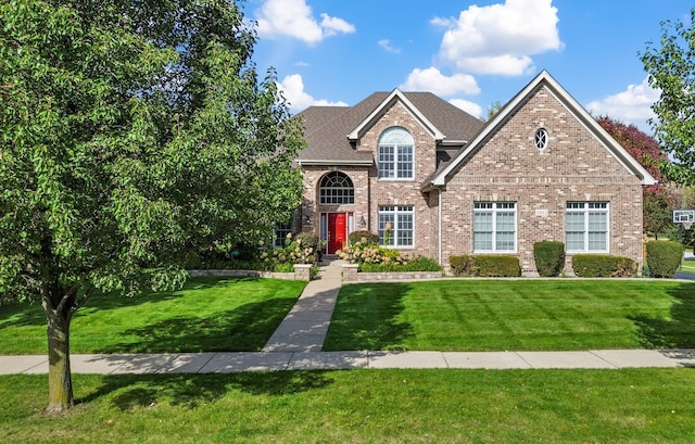 traditional-style home featuring brick siding, a front lawn, and roof with shingles