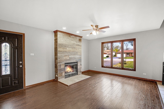 unfurnished living room featuring dark hardwood / wood-style floors, ceiling fan, and a tiled fireplace