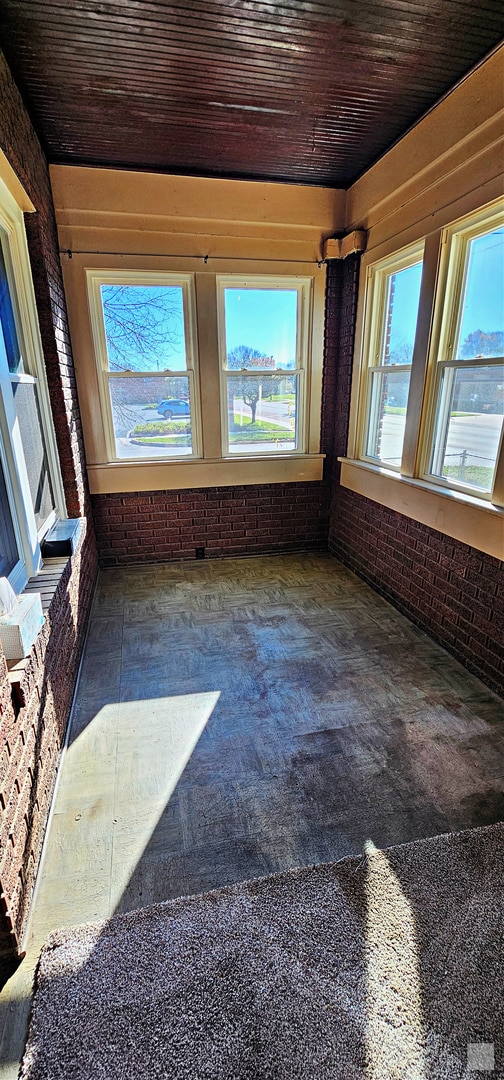 carpeted spare room with wood ceiling and brick wall