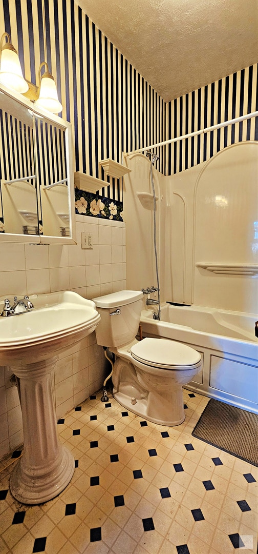 bathroom with toilet, shower / tub combination, a textured ceiling, and tile walls