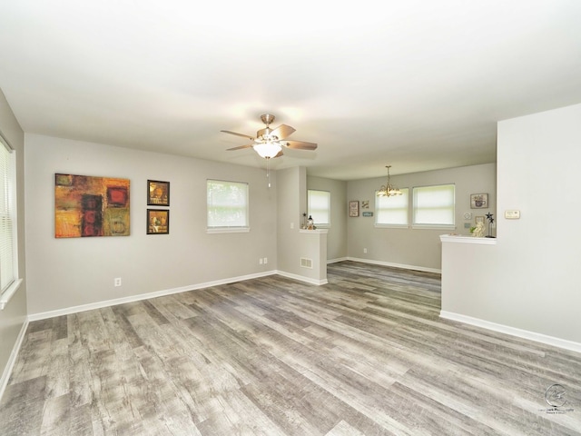 spare room with wood-type flooring, a healthy amount of sunlight, and ceiling fan with notable chandelier