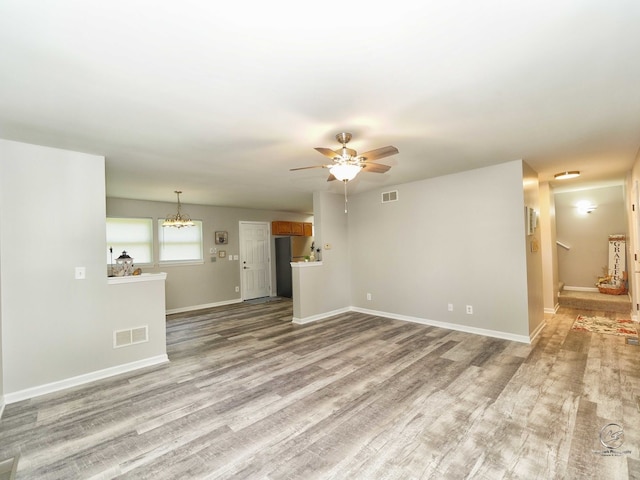 unfurnished living room featuring ceiling fan with notable chandelier and light hardwood / wood-style flooring