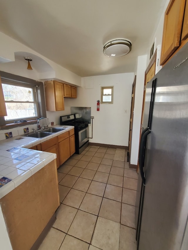 kitchen with tile counters, sink, light tile patterned flooring, and stainless steel appliances