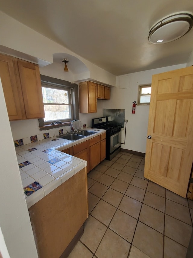 kitchen featuring light tile patterned floors, gas stove, tile counters, and sink