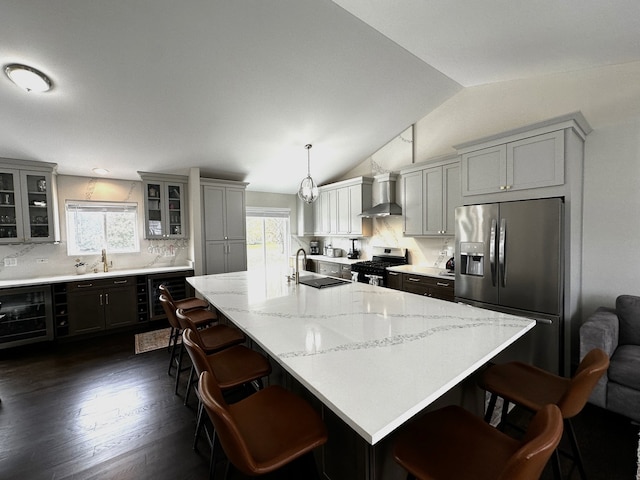 kitchen featuring wall chimney exhaust hood, stainless steel appliances, vaulted ceiling, sink, and pendant lighting