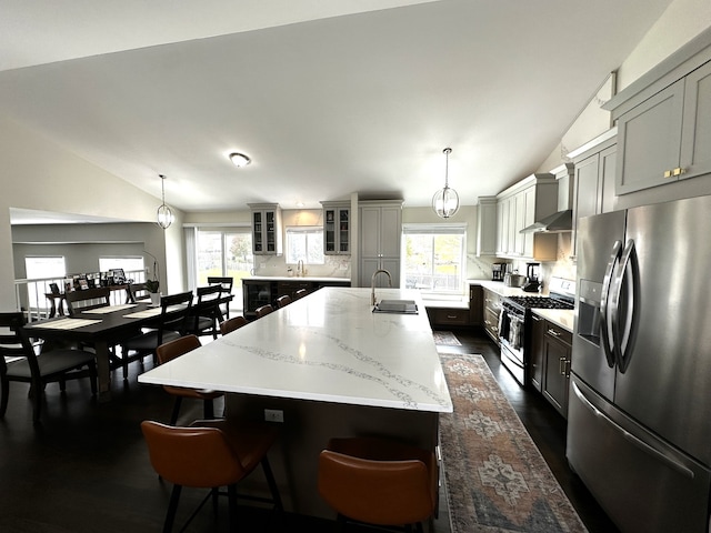 kitchen with a large island with sink, hanging light fixtures, stainless steel appliances, and vaulted ceiling