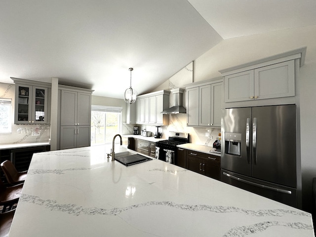 kitchen featuring a kitchen bar, appliances with stainless steel finishes, wall chimney exhaust hood, sink, and pendant lighting