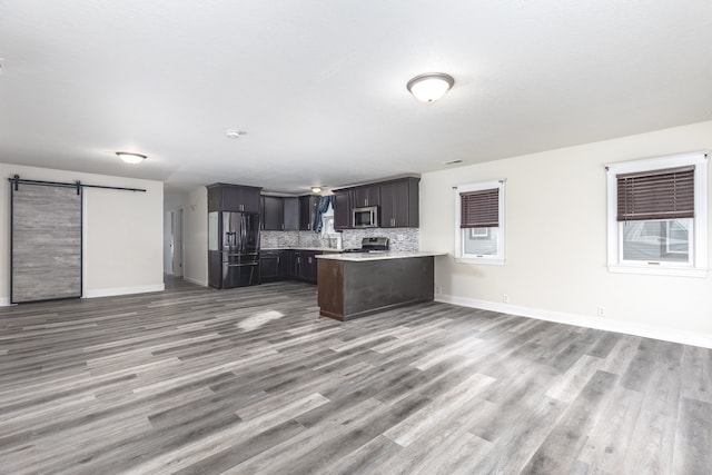 kitchen with kitchen peninsula, backsplash, stainless steel appliances, a barn door, and hardwood / wood-style floors