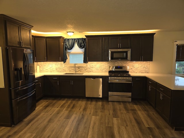 kitchen featuring kitchen peninsula, appliances with stainless steel finishes, decorative backsplash, sink, and dark hardwood / wood-style floors