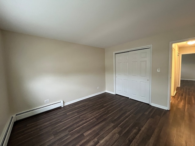 unfurnished bedroom with baseboard heating, a closet, and dark wood-type flooring