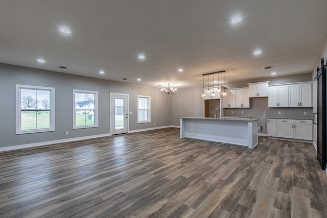 kitchen with dark wood-type flooring, sink, a notable chandelier, white cabinets, and an island with sink