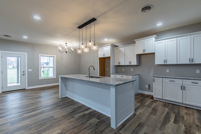 kitchen with white cabinetry, sink, hanging light fixtures, dark hardwood / wood-style floors, and a kitchen island with sink