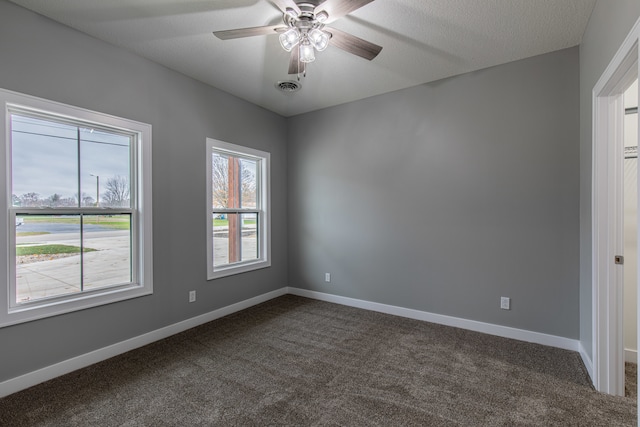 spare room with a textured ceiling, dark carpet, and ceiling fan