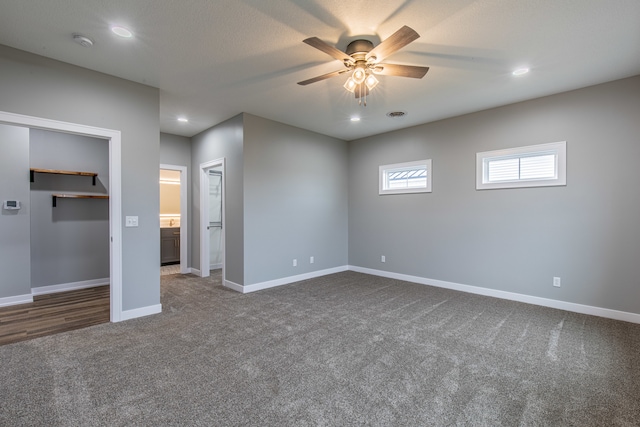 unfurnished bedroom with dark carpet, ceiling fan, a spacious closet, connected bathroom, and a closet