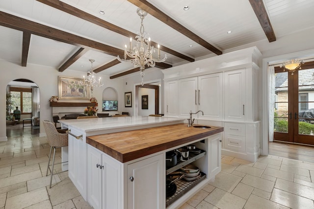 kitchen featuring wooden counters, a large island with sink, white cabinets, and hanging light fixtures