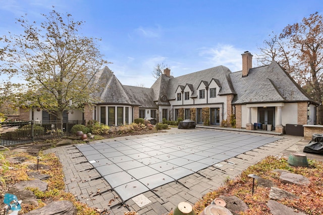 rear view of property featuring a covered pool and a patio area