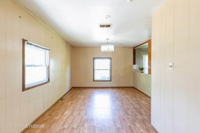 unfurnished room featuring a notable chandelier, light wood-type flooring, and wooden walls