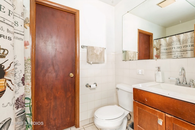 bathroom with toilet, vanity, tile patterned floors, and tile walls