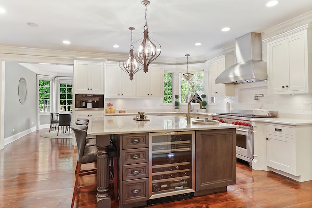 kitchen with wall chimney exhaust hood, plenty of natural light, a kitchen island with sink, and beverage cooler