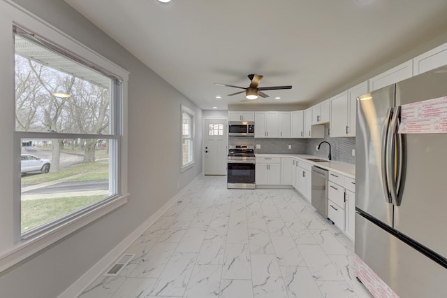 kitchen with white cabinetry, sink, ceiling fan, stainless steel appliances, and backsplash