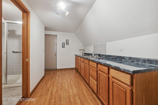 kitchen featuring light hardwood / wood-style floors, lofted ceiling, sink, and dark stone counters